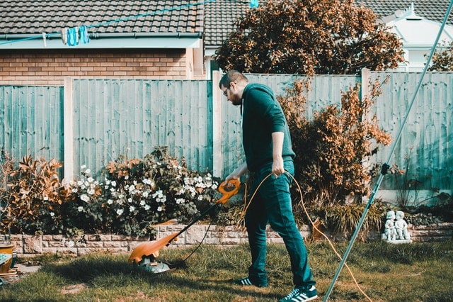man-holding-orange-electric-grass-cutter-on-lawn